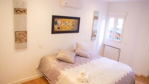 Quarto com uma cama grande, roupa de cama estampada, uma obra de arte emoldurada e uma janela com vista.