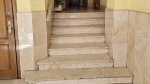 Um conjunto de degraus de mármore leva a uma porta, com uma planta em vaso à esquerda e um espelho de porta de madeira à direita.