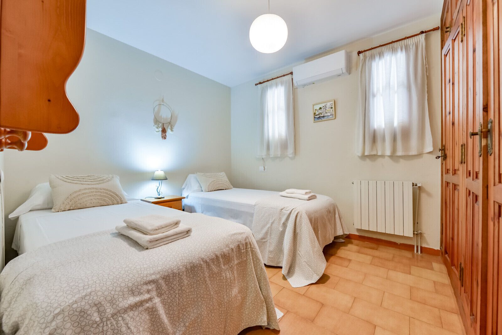 A room with two beds, a nightstand, a lamp, a radiator, and a wooden wardrobe.