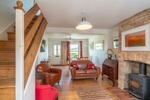A cozy living room with a fireplace, wooden staircase, leather furniture, and a dining area with curtains. - Fantastic location, Cambridge. Lovely cottage in Grantchester village (Cambridge)