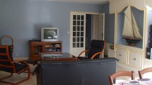 A living room with a television on a wooden stand, a sailboat model, and a door leading to another room. - House with garden  3 stars (Névez)