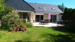 A house with a stone exterior, a covered patio with a table and chairs, and a garden with pink flowers. - House with garden  3 stars (Névez)