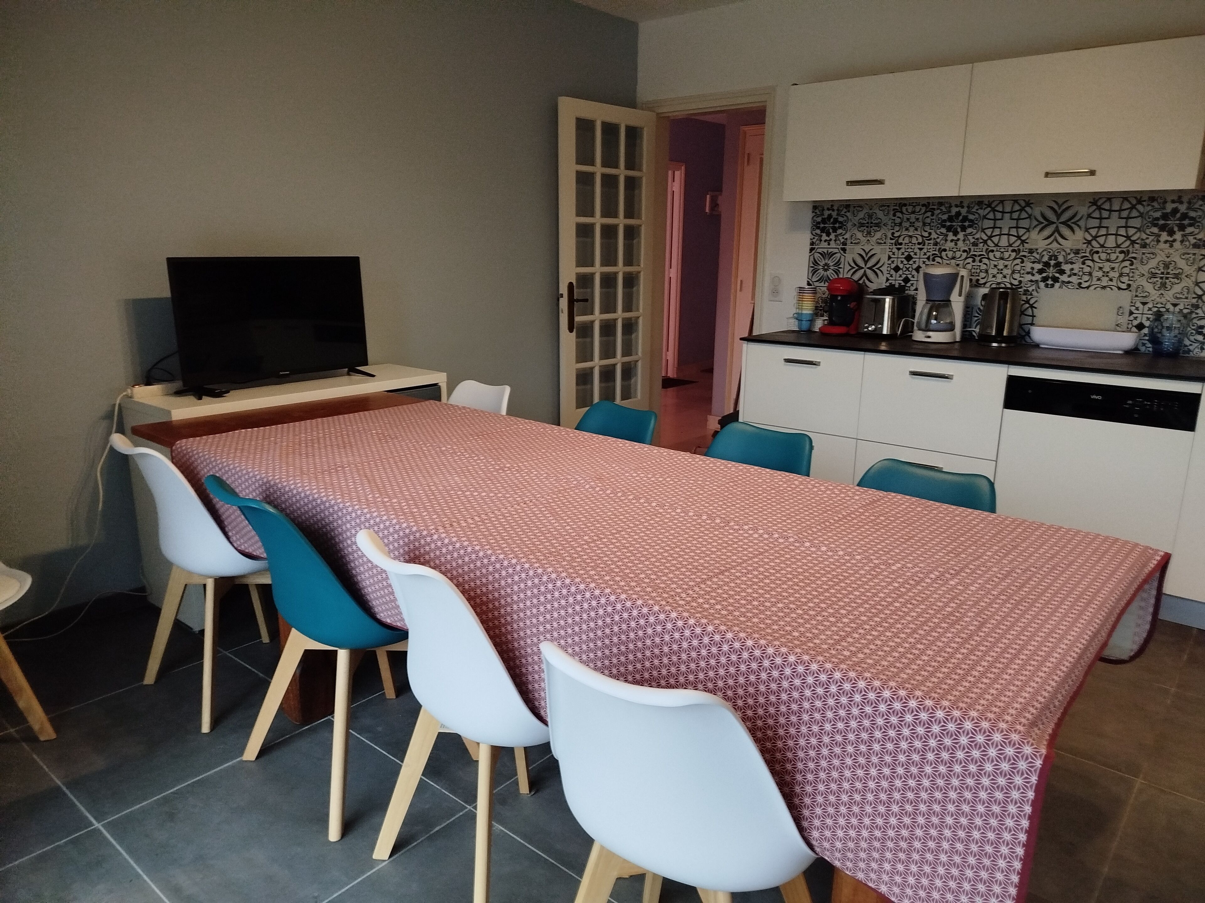 A compact kitchen with white cabinets, a tiled backsplash, and a dining area with a table and chairs.