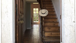 Een houten trap met een hoed aan de leuning, een betegelde vloer en een deur met een lamp erboven.