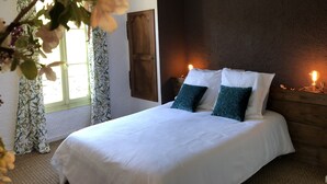 Een slaapkamer met een groot bed, twee kussens, een houten hoofdbord, een nachtkastje en een raam met gordijnen.
