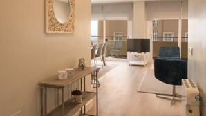 Ein modernes Wohnzimmer mit einem großen Spiegel, einem Fernseher, einem blauen Sessel und einem Essbereich mit Stühlen und einem Tisch.