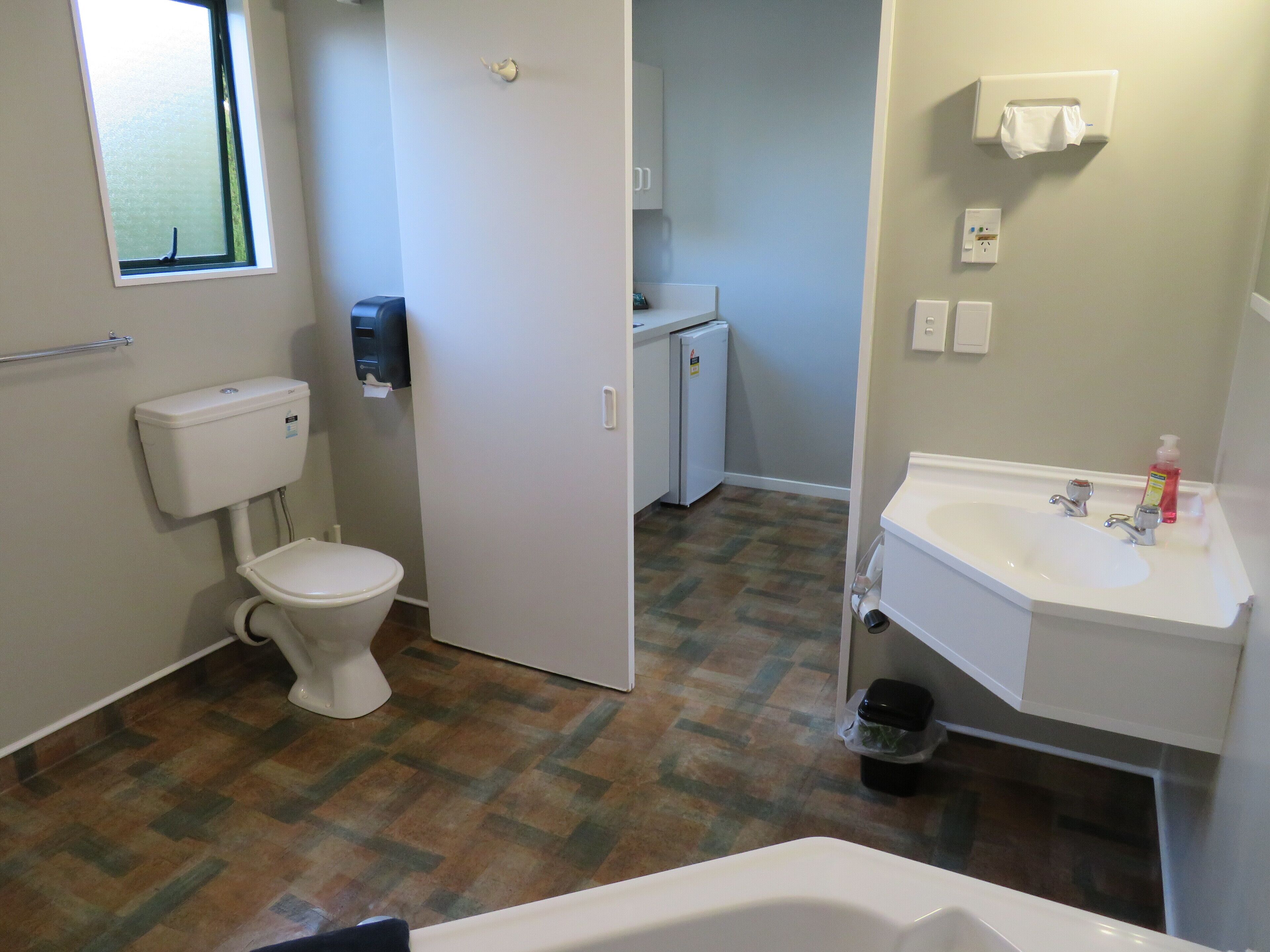 Een badkamer met toilet, wastafel en een kleine koelkast.