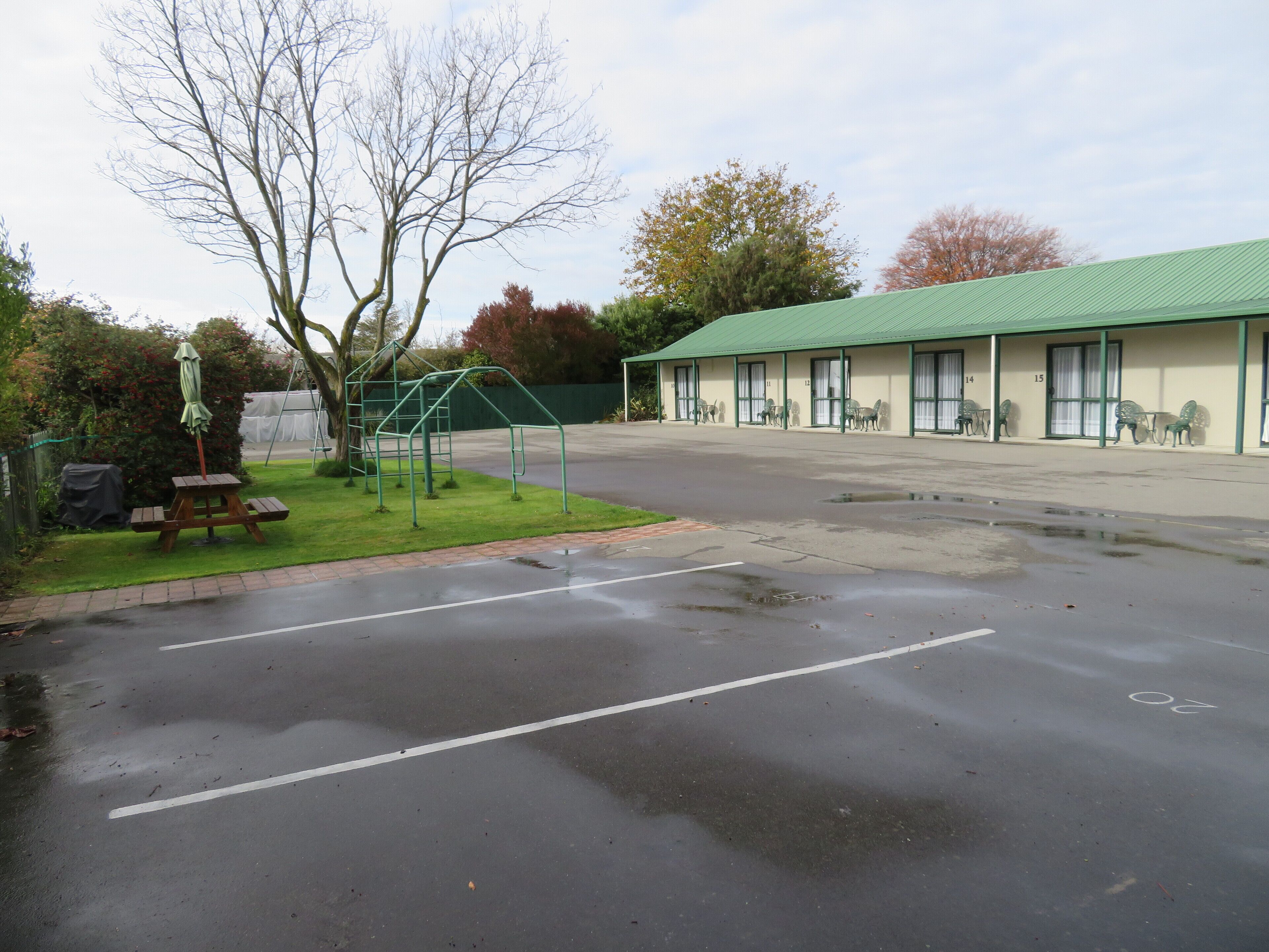 Un motel con techo verde, mobiliario exterior y un parque infantil.