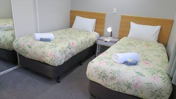 Una habitación de hotel con dos camas individuales, cada una con ropa de cama floral y un cabecero de madera. Hay una mesita de noche con una lámpara entre las camas.