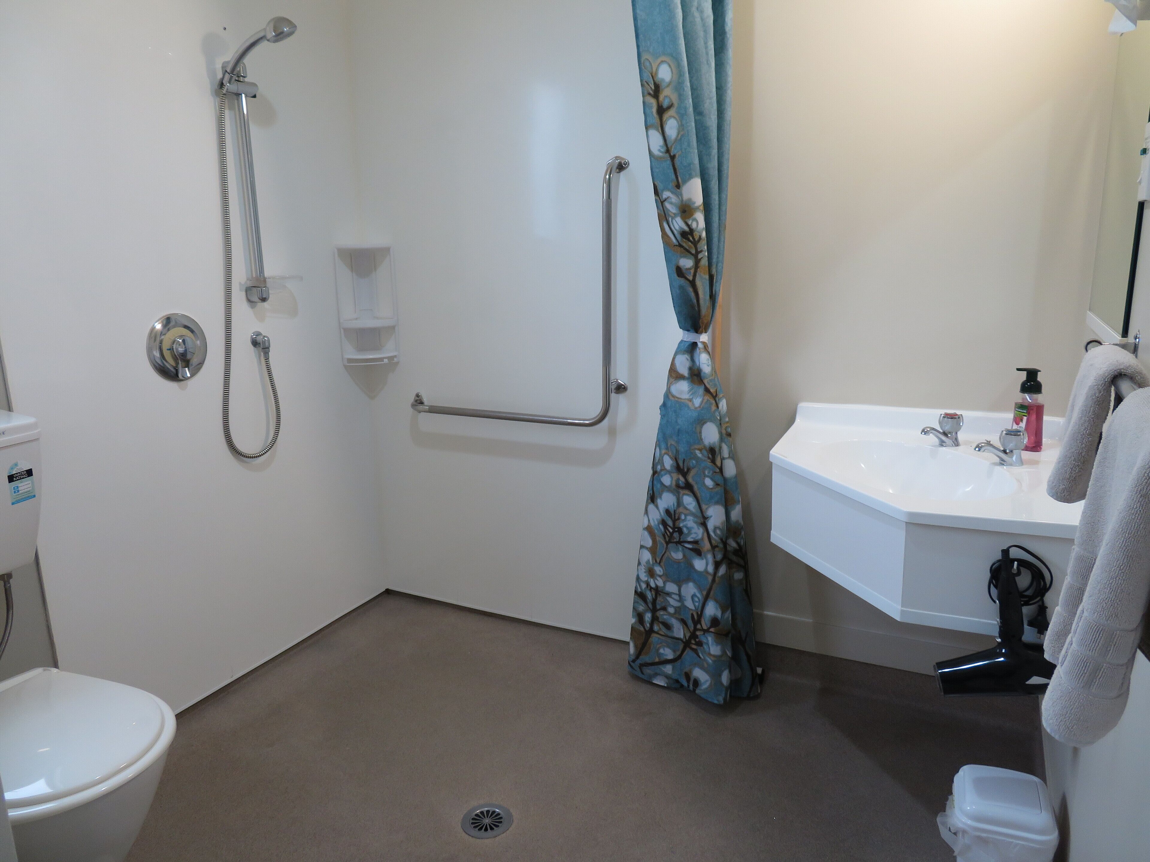 A bathroom with a shower, toilet, sink, and grab bars.