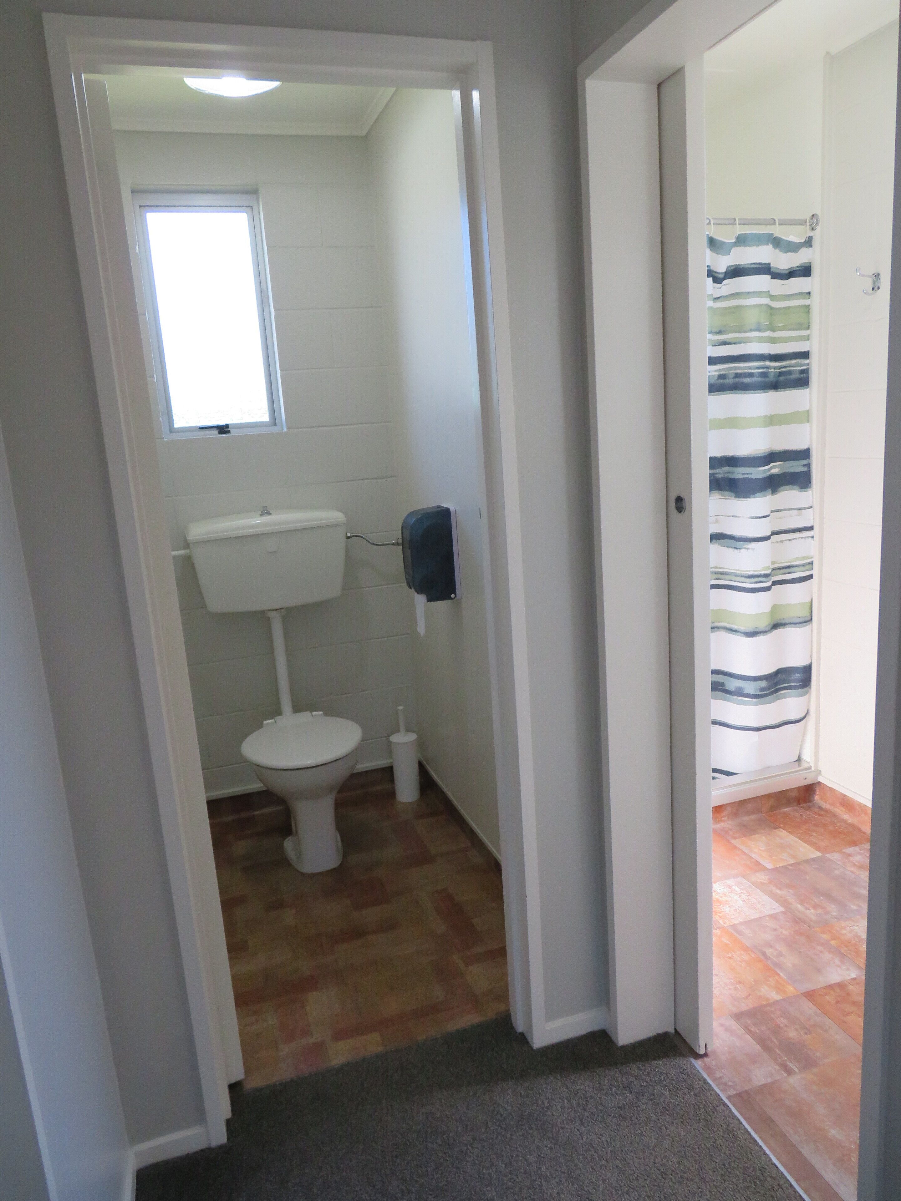 Un baño con inodoro, secador de manos y cortina de ducha a rayas.