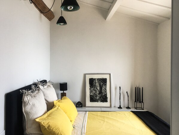 A bedroom with a bed, pillows, a framed artwork, a bedside table with a lamp, and a wall-mounted light fixture. - House in Grimaldi. Spectacular view on the French Riviera with rooftop terrace! (Grimaldi Superiore (Ventimiglia))