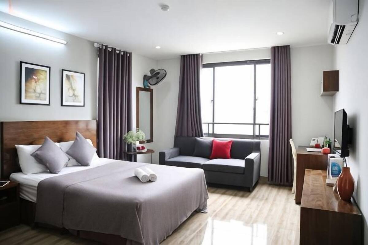 A hotel room with a bed, a sofa, a desk, a TV, and a large window.