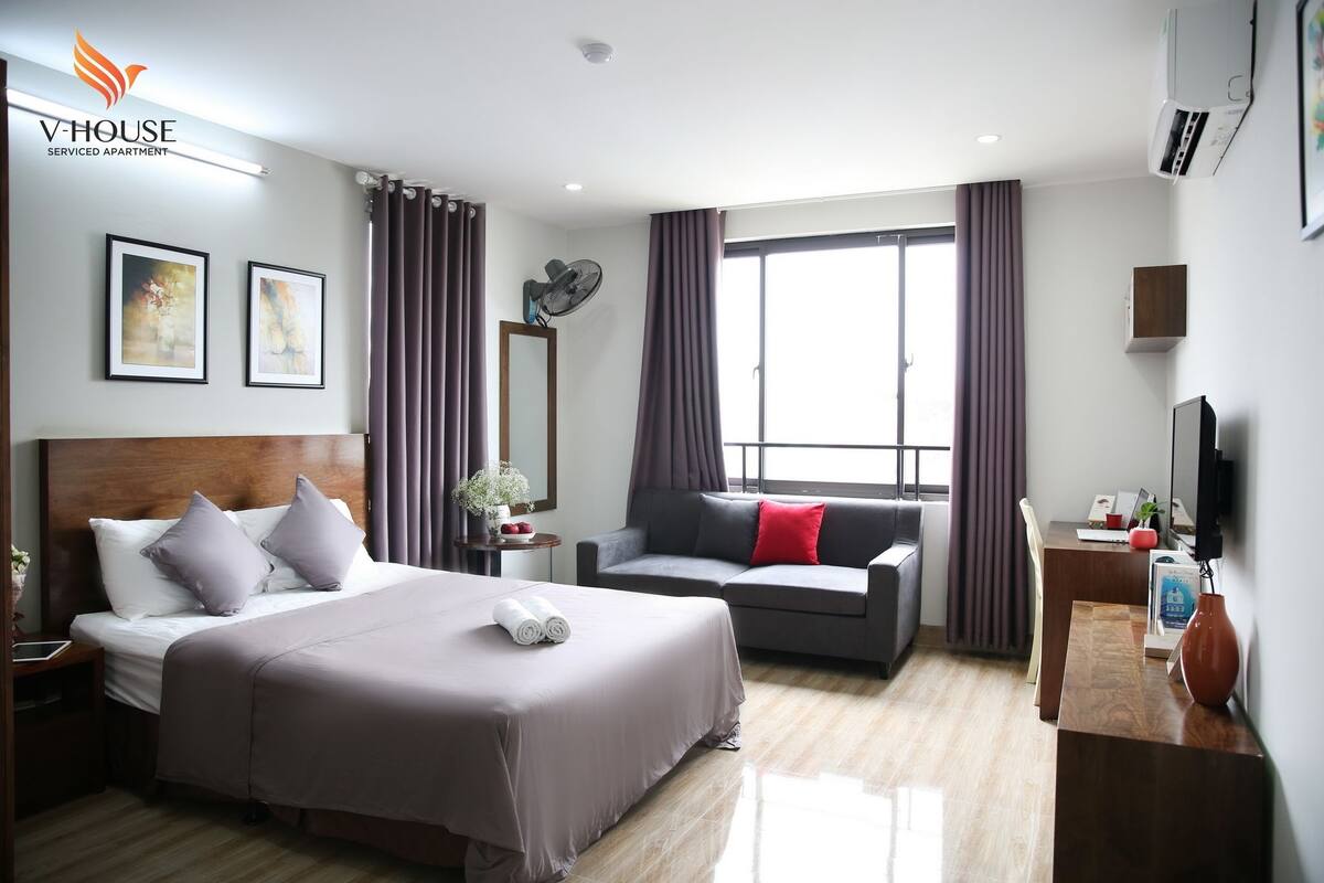 A hotel room with a bed, a sofa, a desk, a TV, and a window with curtains.