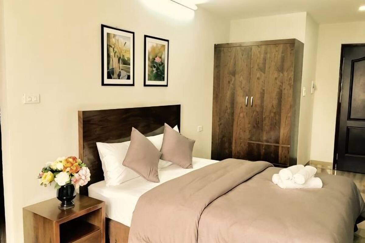 A bedroom with a bed, a nightstand, a wooden wardrobe, and two framed pictures on the wall.