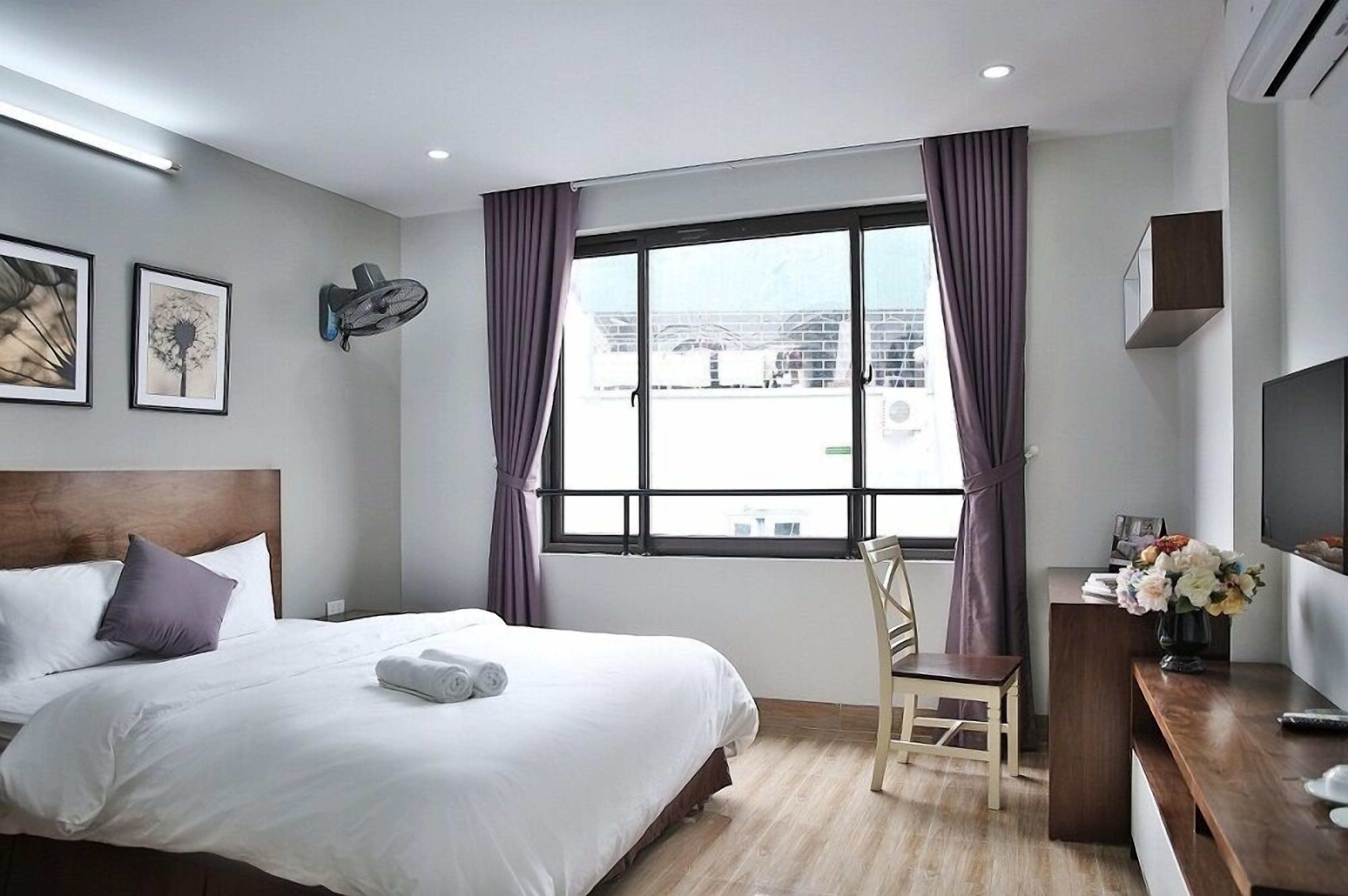 Een hotelkamer met een groot bed, een bureau met stoel, een televisie en een raam met gordijnen.