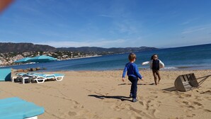 A beach with sun loungers and umbrellas, a clear sky, and a view of the sea and distant buildings. - Very nice spacious and bright apartment T3 any comfort (terrace 25m2) (Hyères)