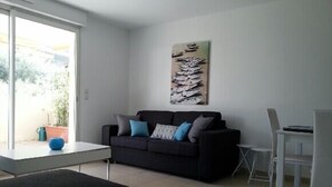 A modern living room with a black sofa, blue cushions, a white coffee table, and a painting on the wall. - Very nice spacious and bright apartment T3 any comfort (terrace 25m2) (Hyères)