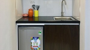 A compact kitchen with a microwave, a sink, and a small refrigerator. - V House 1 Serviced Apartment (Hanoi)