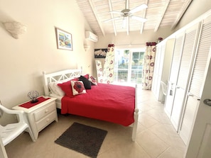 A bedroom with a bed, a nightstand, a chair, a window with curtains, and a ceiling fan. - 3 Bed Villa with Private Pool, West Coast Barbados (Porters St James)
