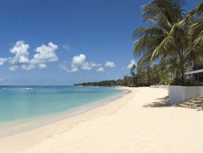A beach with clear turquoise water, white sand, and palm trees.