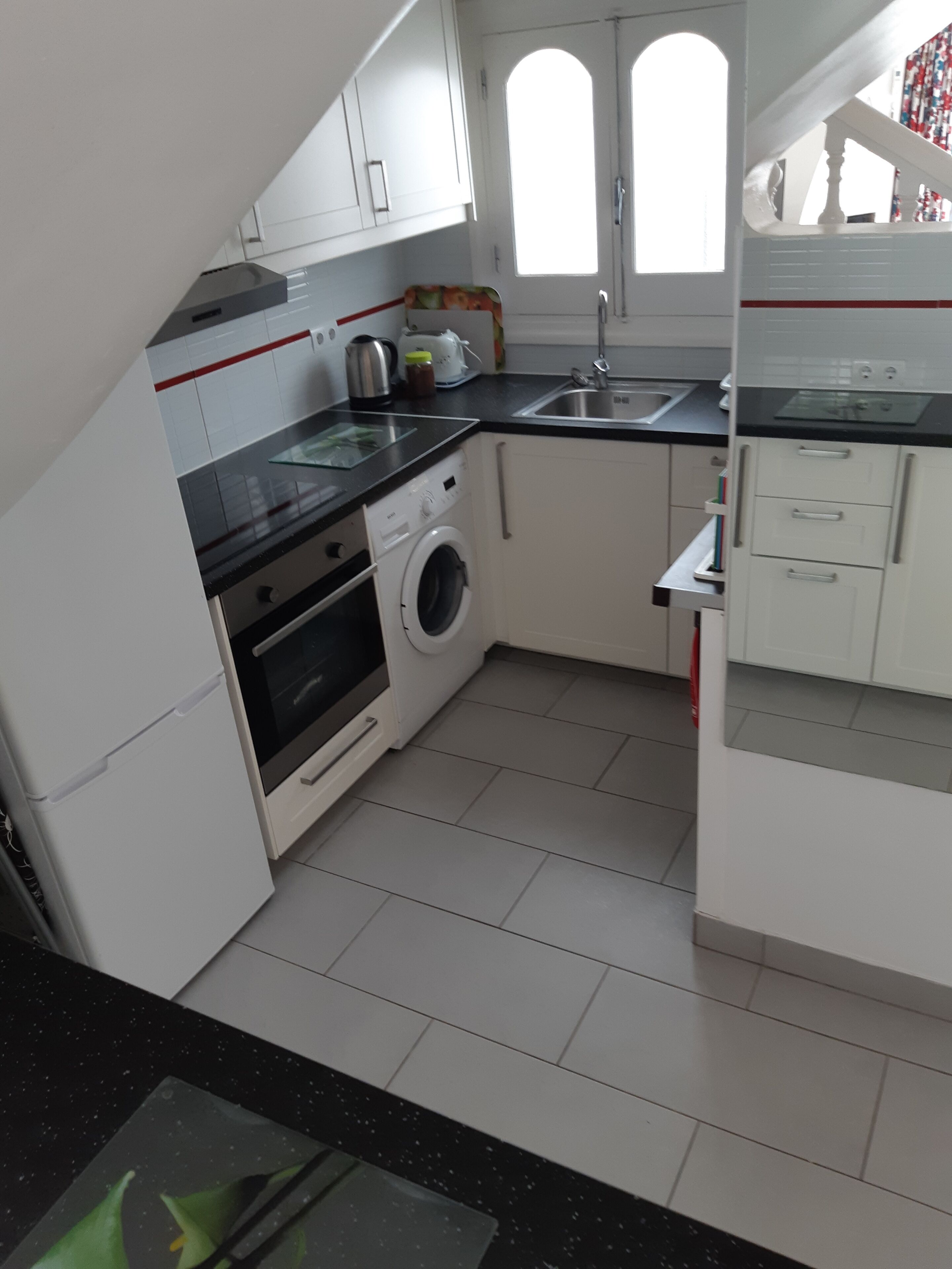 A compact kitchen with white cabinets, a washing machine, a stove, and a sink.