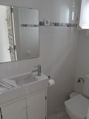 Une salle de bain avec un lavabo blanc, un miroir, des toilettes et un porte-serviettes.