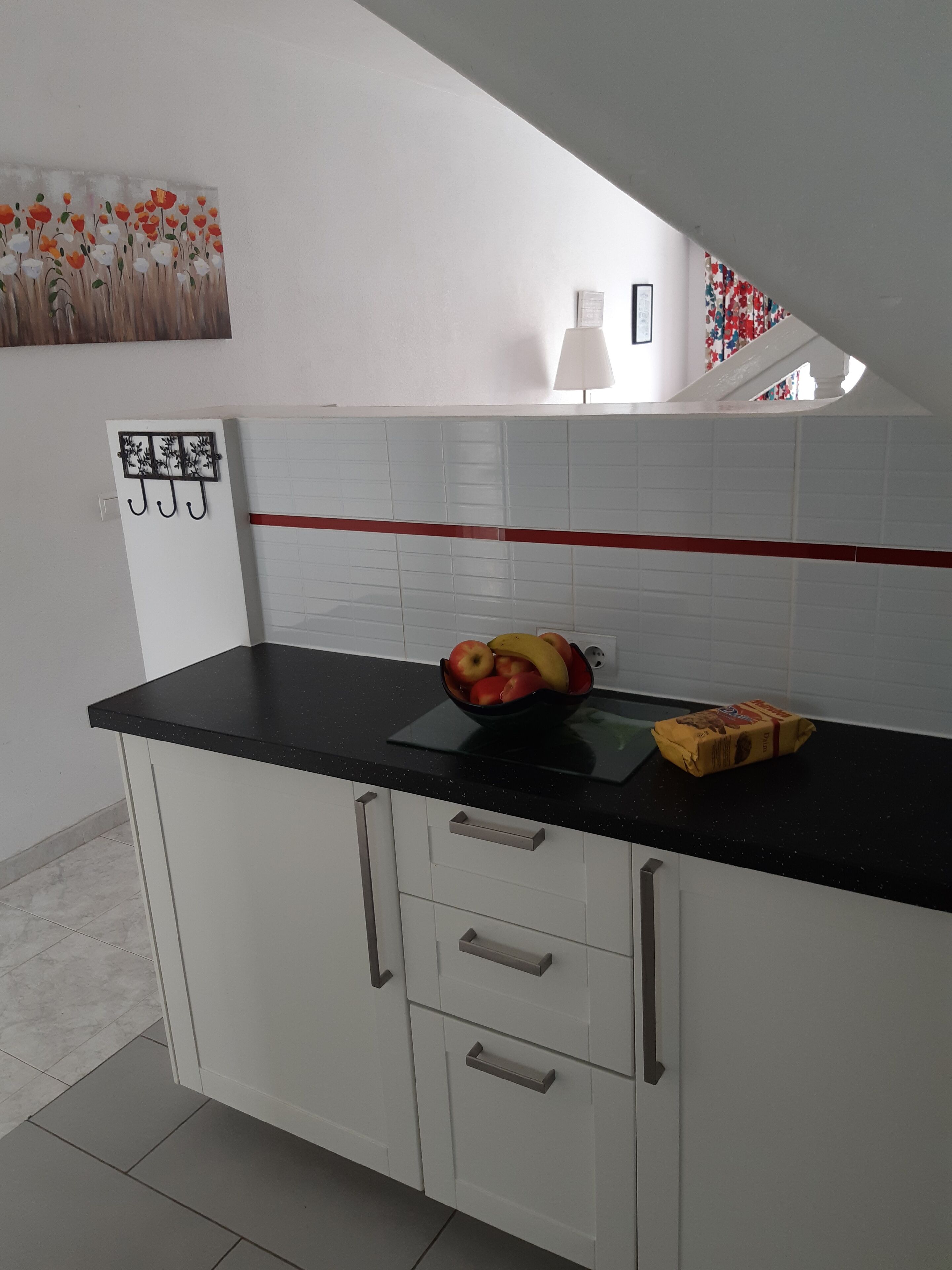A kitchen with white cabinets, a black countertop, and a fruit bowl containing apples and bananas.