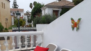 Un ensemble de chaises longues est placé devant un mur blanc orné d’un motif de papillon décoratif, avec une terrasse carrelée et une vue sur les bâtiments voisins.