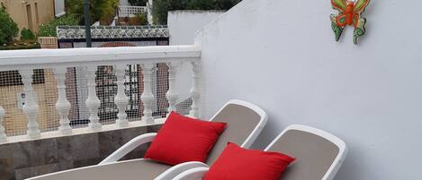 A sun loungers set against a white wall with a decorative butterfly, a tiled patio, and a view of neighboring buildings.