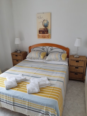 Una cama bien hecha con ropa de cama a rayas y dos almohadas, una obra de arte con un globo terráqueo en la pared y dos mesitas de noche con lámparas.