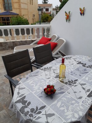 Un patio al aire libre con una mesa preparada para dos personas, con mantel floreado, una botella de vino y un cuenco de fresas.