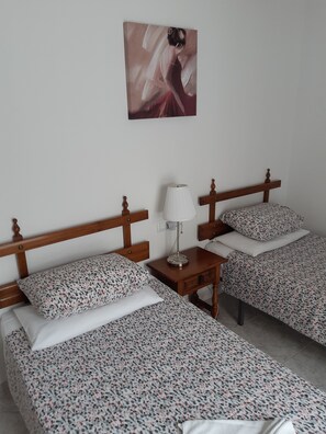 Une chambre d’hôtel avec deux lits, chacun recouvert d’une couvre-lit à motifs floraux et agrémenté d’oreillers assortis. Une table de chevet avec une lampe se trouve entre les deux lits. Un tableau est accroché au mur, au-dessus des lits.