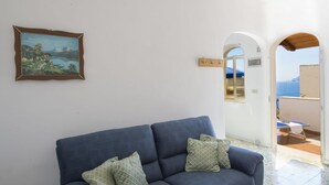 Un divano blu con cuscini a motivi decorativi in una stanza con una parete bianca e un quadro raffigurante un paesaggio.