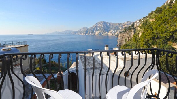 Un balcone con sedie bianche e vista sulla costa.