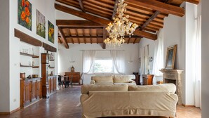 Ein geräumiges Wohnzimmer mit einem großen beigefarbenen Sofa, Holzbalken, einem Kronleuchter und einem Kamin.