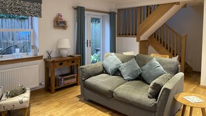A cozy living room with a grey sofa, wooden floor, a small table, a lamp, a bookshelf, and a staircase. - Cottage sleeps 4 with private hot tub. Edinburgh festival less than 1hr away.  (Kinross)