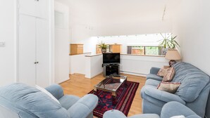 Una sala de estar con un sofá, una mesa de centro y un televisor. Se ve una ventana con vistas al exterior.