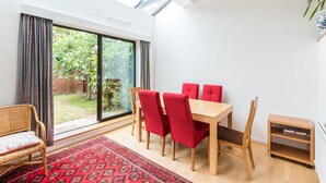 Un comedor con una mesa y sillas, una alfombra roja y vistas a un jardín a través de un vidrio.