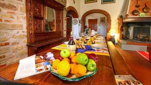 Un espace repas avec une longue table dressée pour le repas, entouré de murs en pierre et de poutres en bois.