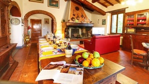 Un coin repas rustique avec une longue table en bois dressée pour le repas, une cheminée et un espace cuisine doté de meubles en bois.