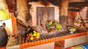 Une cheminée rustique en briques, agrémentée d’un panier et de fleurs sur le manteau, et entourée de fruits et de verres à vin.