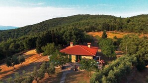 Une maison avec un toit rouge, entourée d’arbres et de collines.