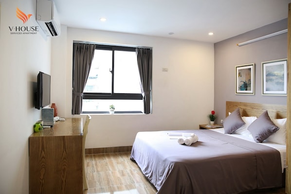 A bedroom with a bed, a desk, a TV, and a window with curtains.