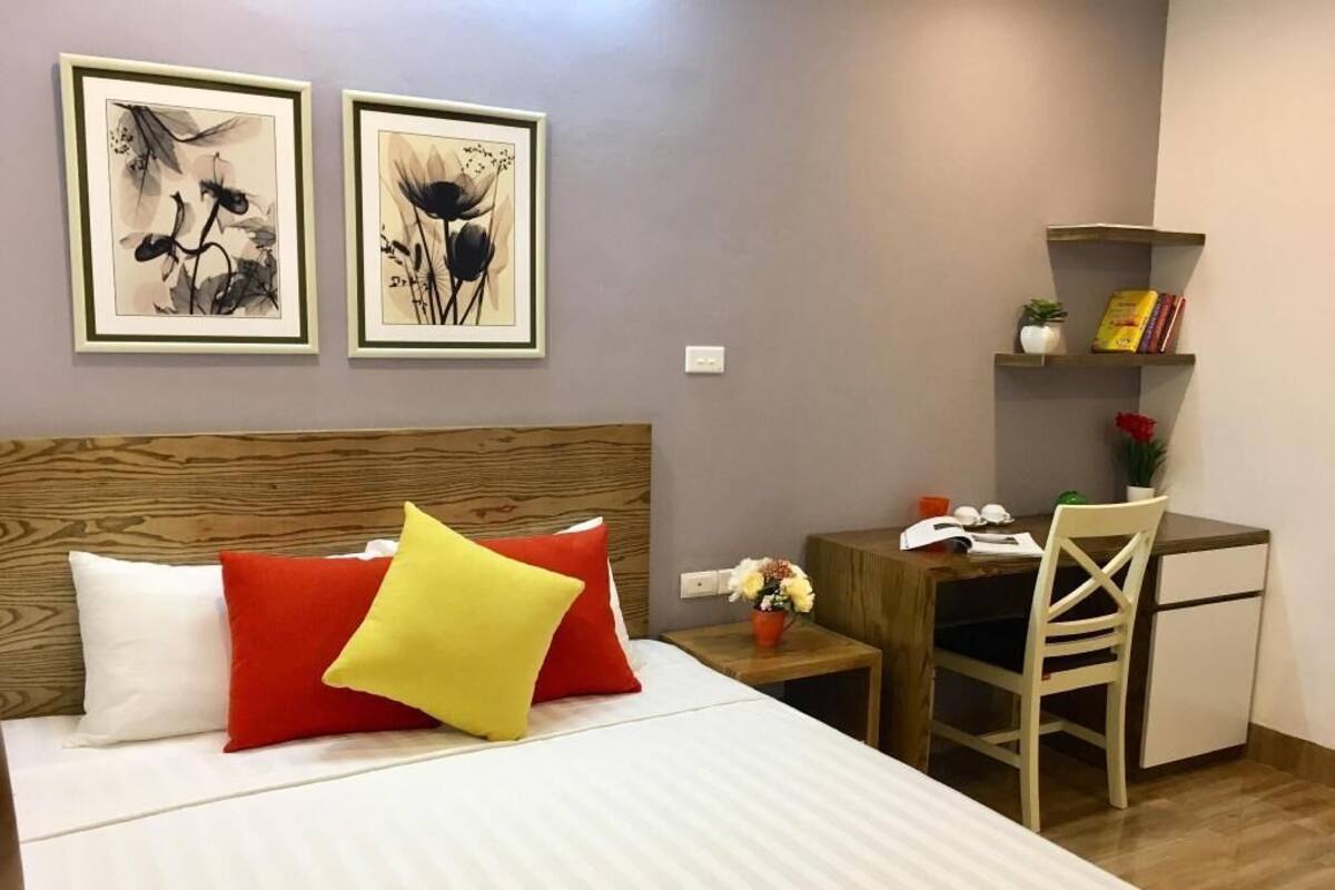 A neatly arranged room with a bed, a desk, a chair, and two framed artworks on the wall.