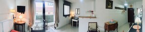 A room with a dining area, a small table with a chair, a TV mounted on the wall, and a window with curtains.