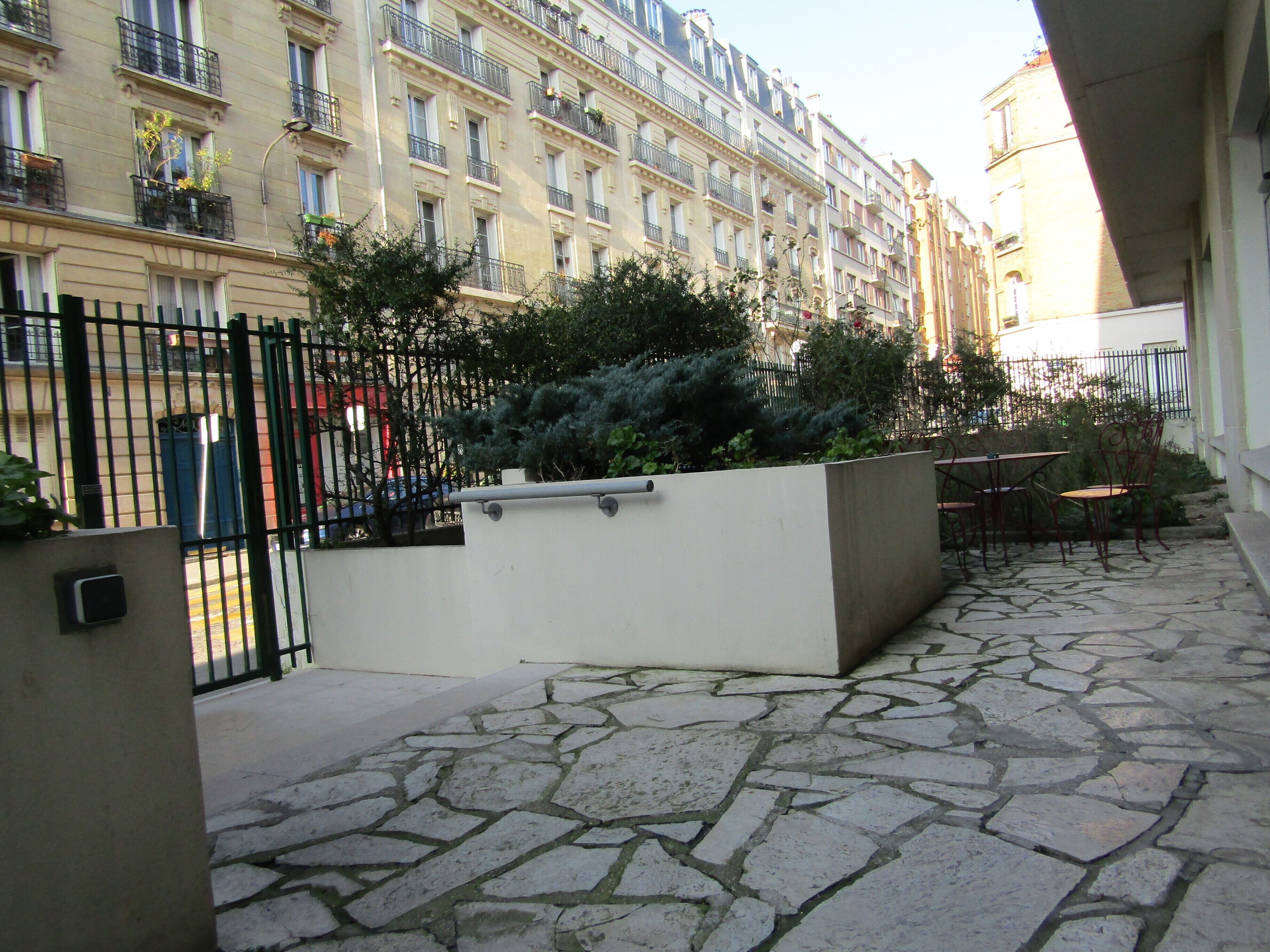 Une cour avec un sol en pierre, une clôture en métal et un jardinier agrémenté de plantes vertes.