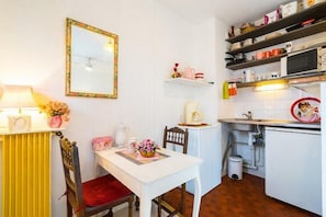 A compact kitchen with white cabinets, a microwave, and a sink. There is a dining table with a chair and a vase of flowers.