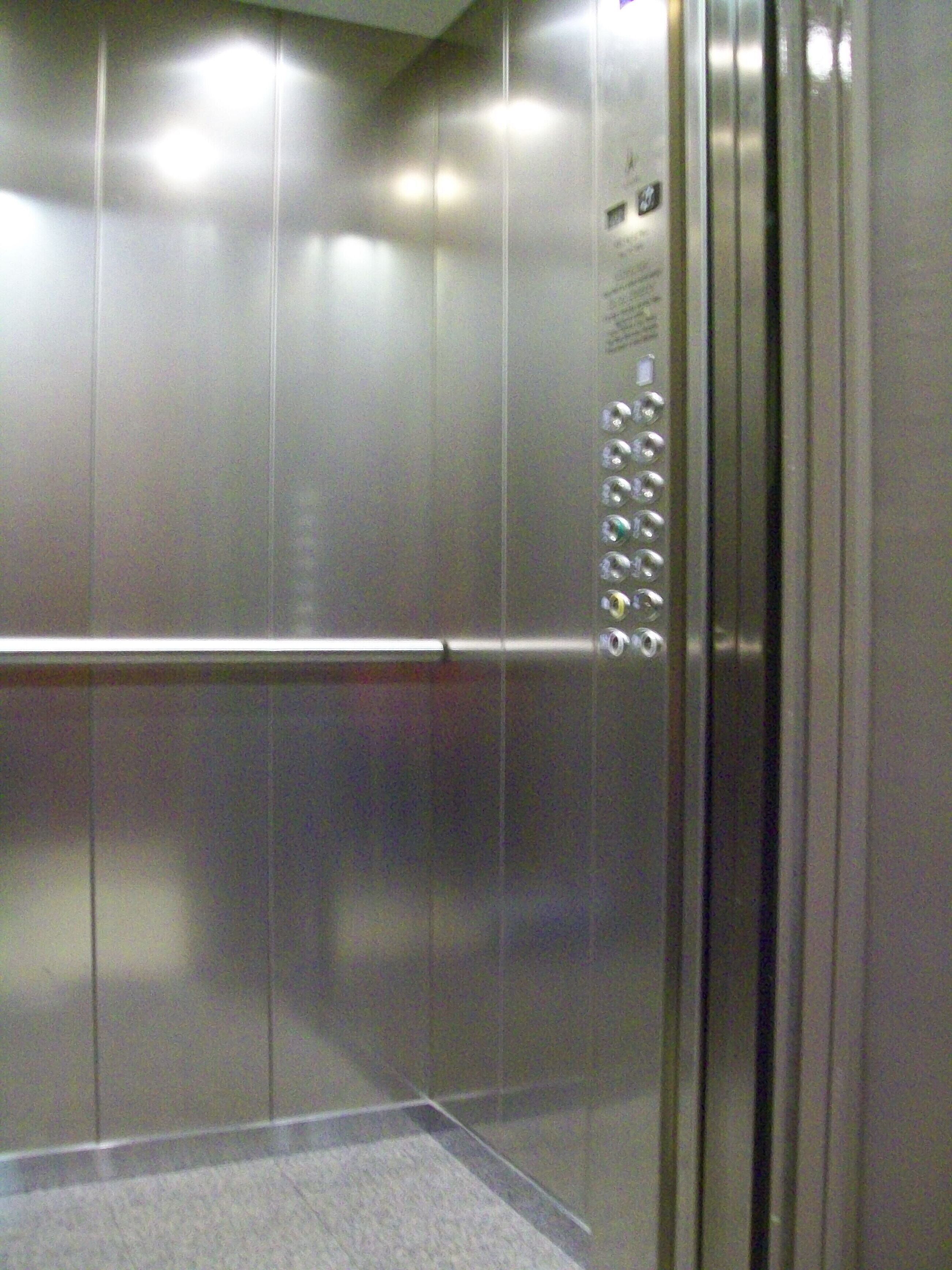 An elevator interior with metallic walls, a handrail, and a control panel with buttons.