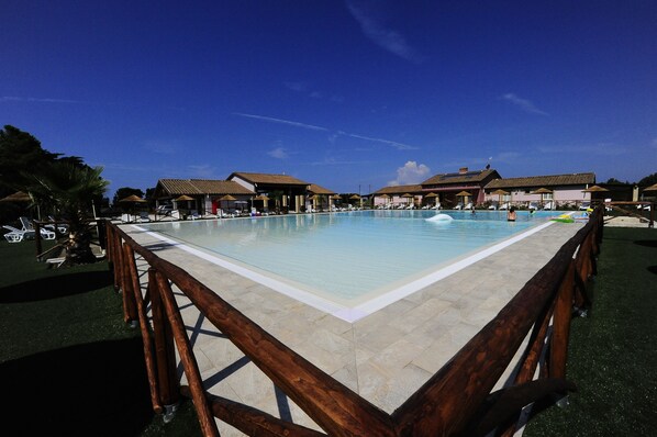 A large outdoor swimming pool with a wooden deck surrounding it, and several beach umbrellas. - Appartamento Palazzeta With Pool, Near the Sea (Cecina)